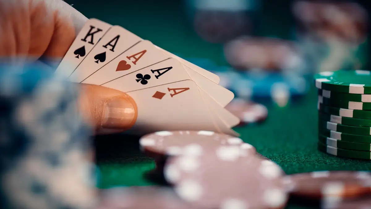 A player's hand fanning a king and three aces above stacks of chips