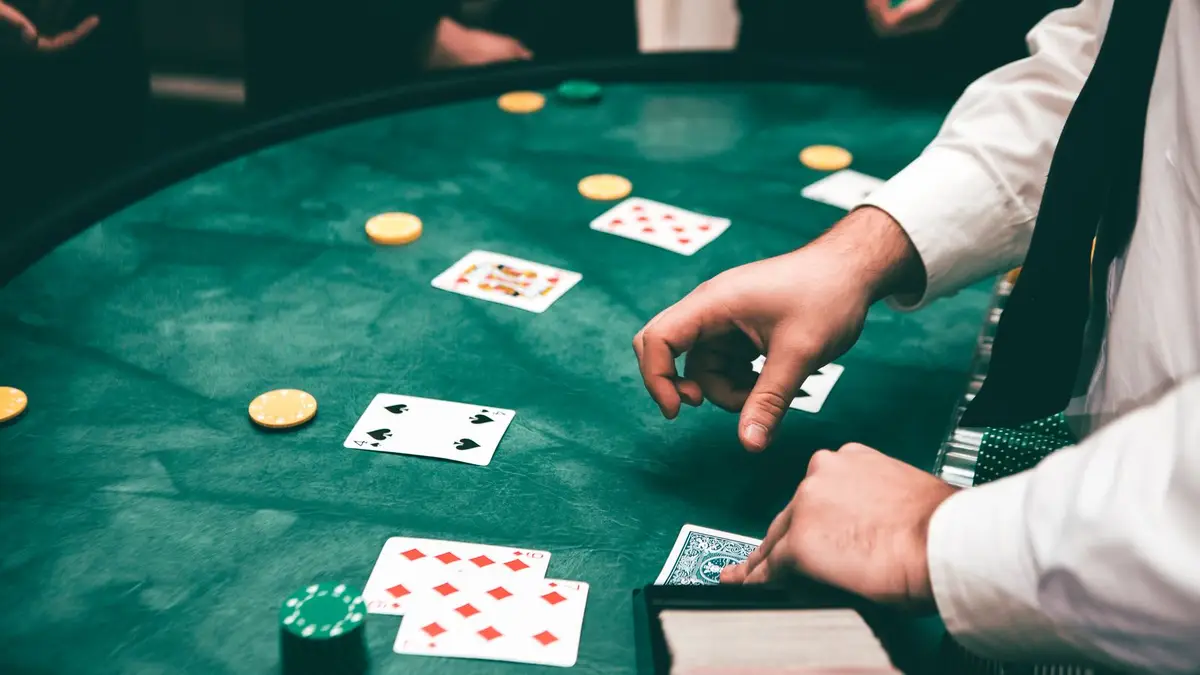 A dealer laying cards on a green felt table mid-hand